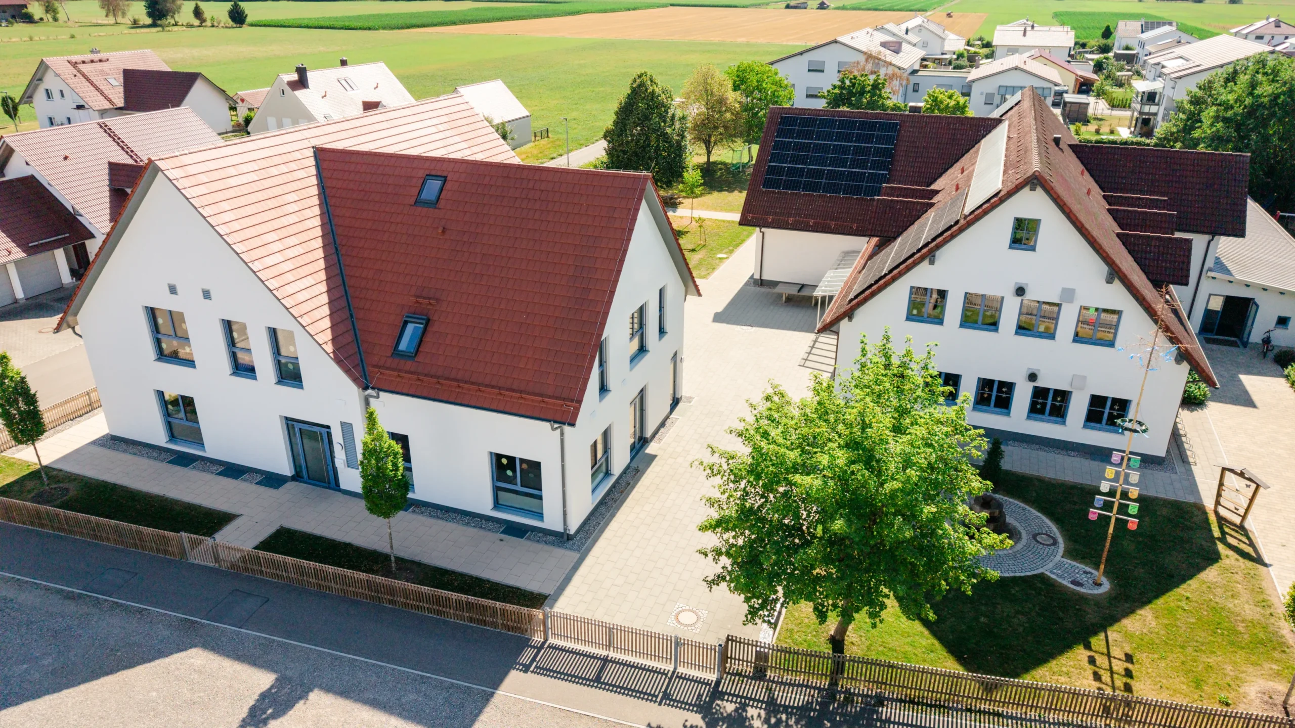 Kinderhort in Rammingen mit zwei Gebäudeteilen und roten Dächern aus der Luft